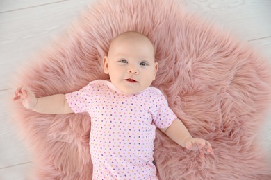 Photo of Adorable baby girl lying on fluffy rug, top view