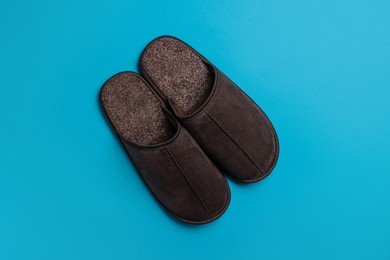 Pair of brown slippers on light blue background, top view