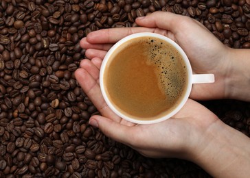 Woman with cup of tasty espresso and roasted coffee beans, top view