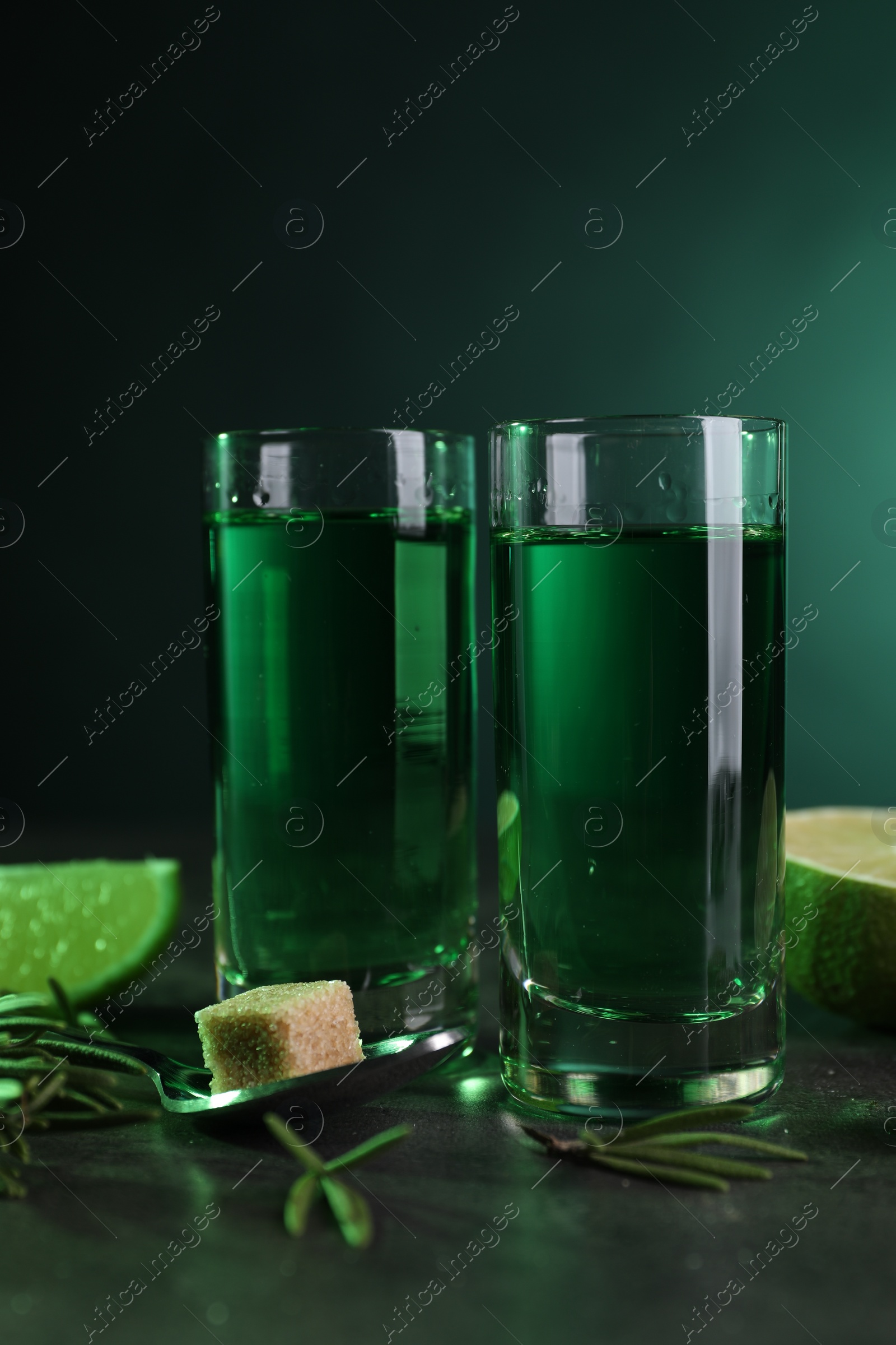 Photo of Absinthe in shot glasses, spoon, brown sugar and rosemary on gray table. Alcoholic drink