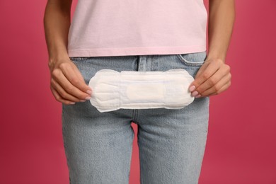 Young woman with menstrual pad on bright pink background, closeup