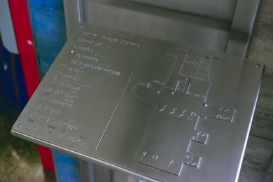 Photo of Silver stand with Braille text and building plan indoors, closeup