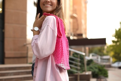 Photo of Young woman with stylish pink net bag on city street, closeup