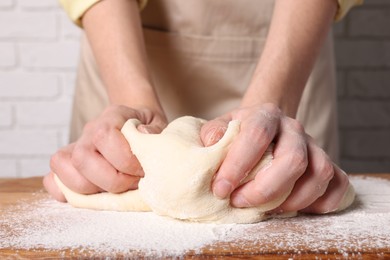 Woman kneading dough at wooden table, closeup