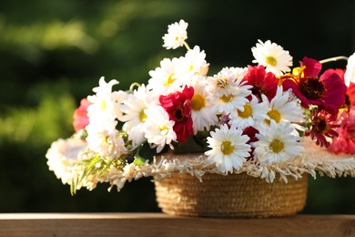 Beautiful wild flowers in wicker basket on wooden table against blurred background
