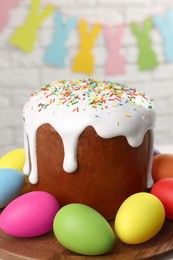 Photo of Tasty Easter cake and decorated eggs on wooden stand, closeup