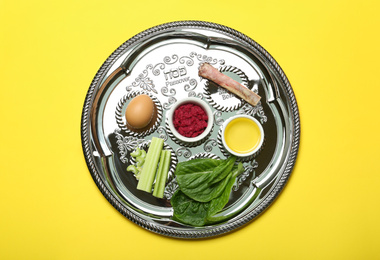 Photo of Passover Seder plate (keara) with symbolic meal on yellow background, top view. Pesah celebration