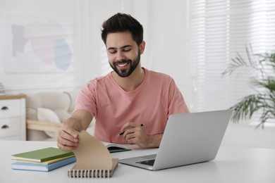 Young man writing down notes during webinar at table in room