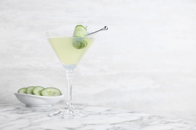 Glass of martini with cucumber on marble table against light background. Space for text
