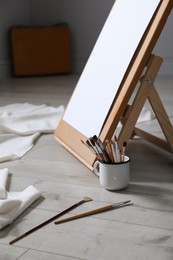 Photo of Different brushes near stand with canvas on floor in artist's studio