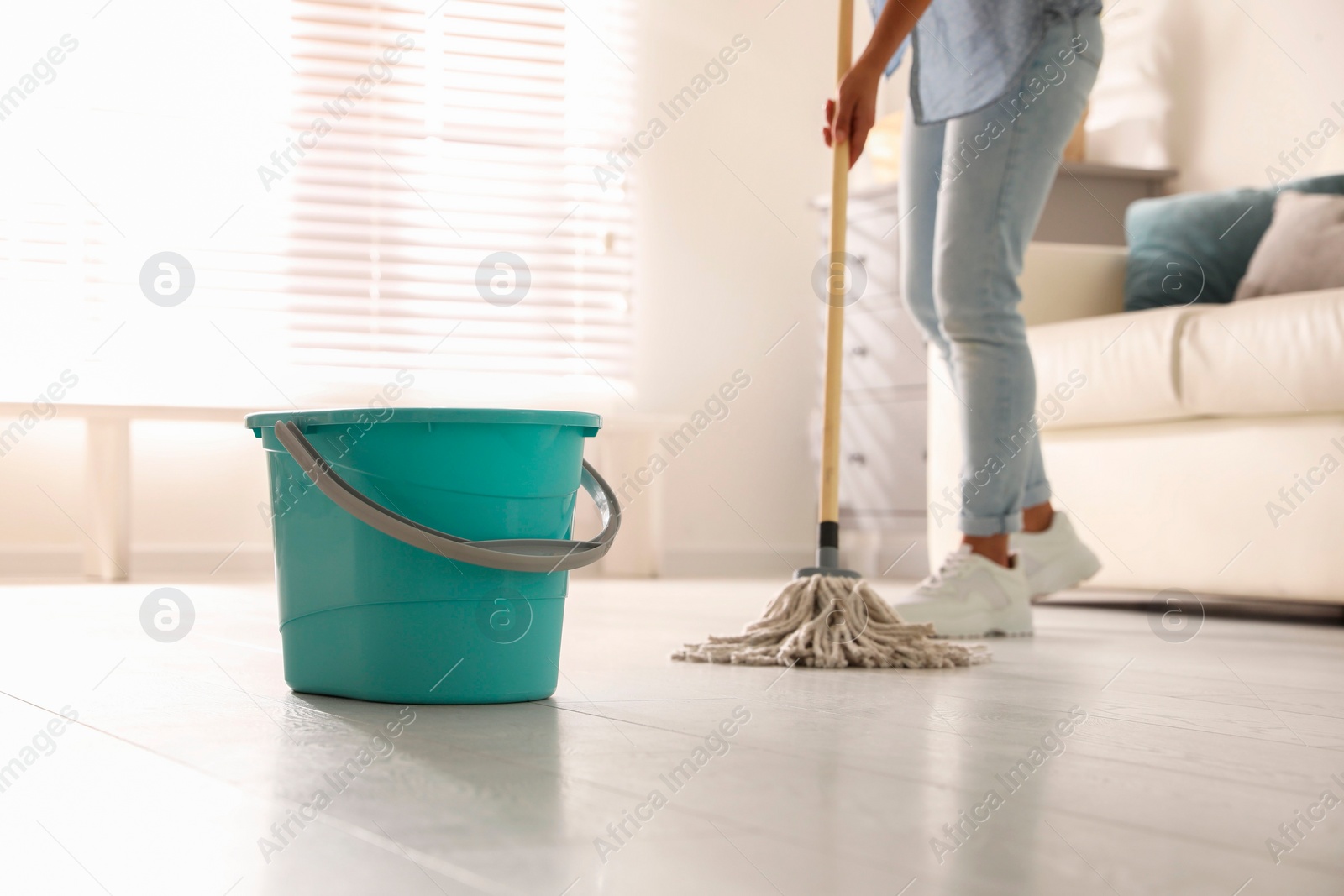Photo of Plastic bucket and woman mopping floor in living room, closeup. Cleaning supplies