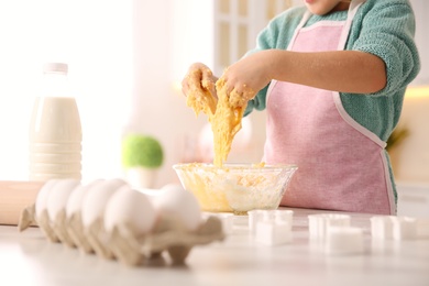 Photo of Little girl making dough at table in kitchen, closeup