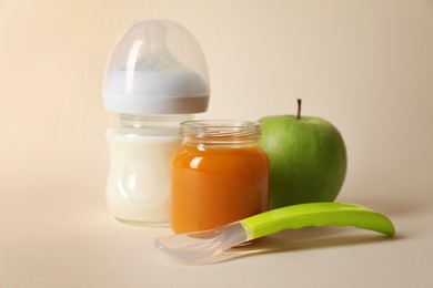 Healthy baby food in jar, bottle of milk, apple and spoon on beige background