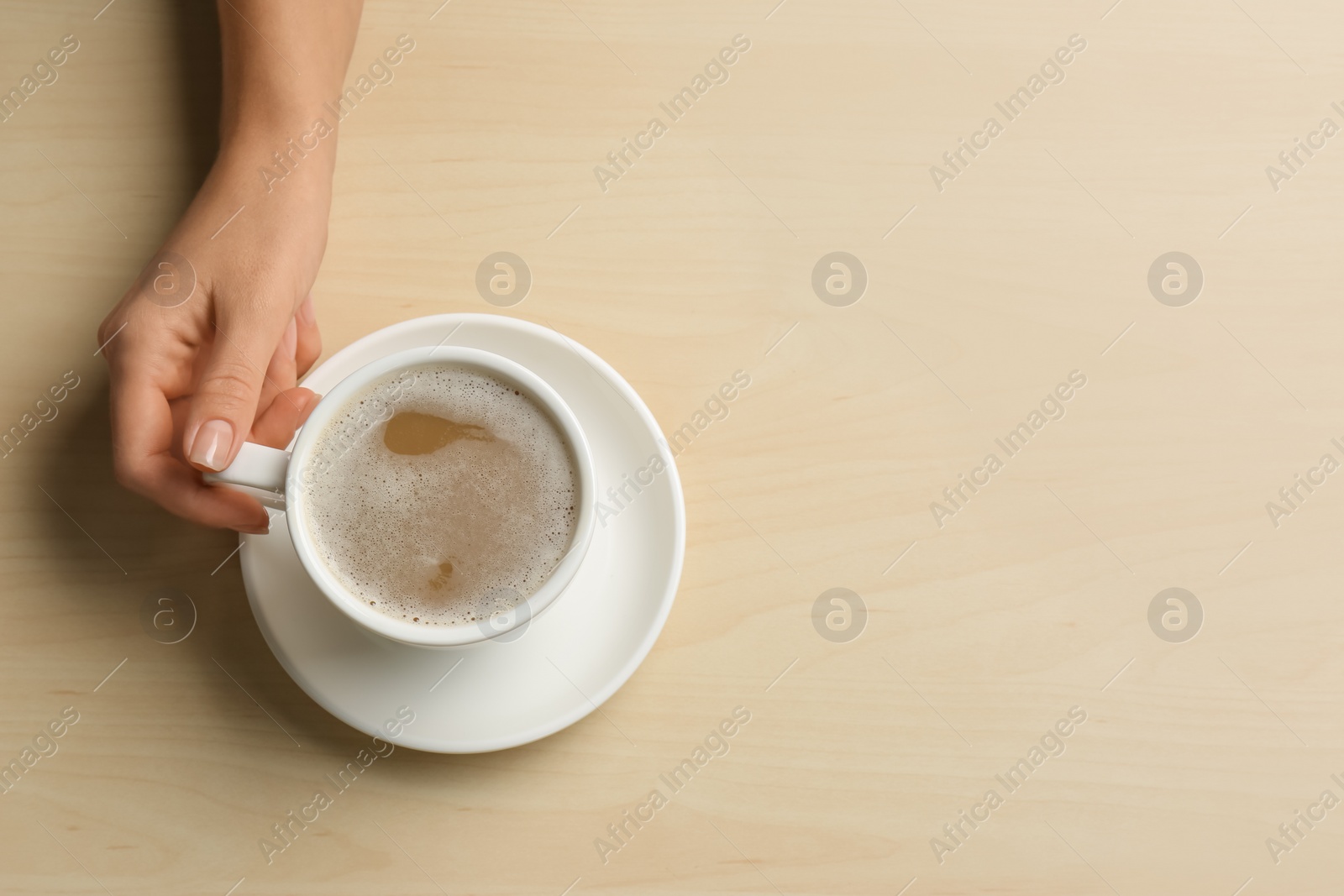 Photo of Woman holding cup of coffee at wooden table, top view. Space for text