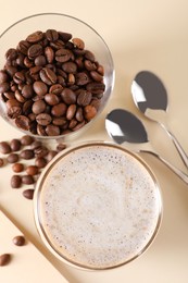 Photo of Refreshing iced coffee with milk in glass, beans and spoons on beige table, flat lay