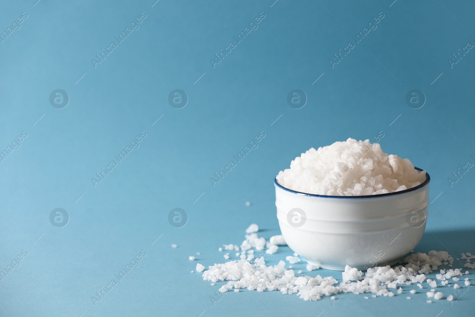 Photo of Organic salt in bowl on light blue background. Space for text