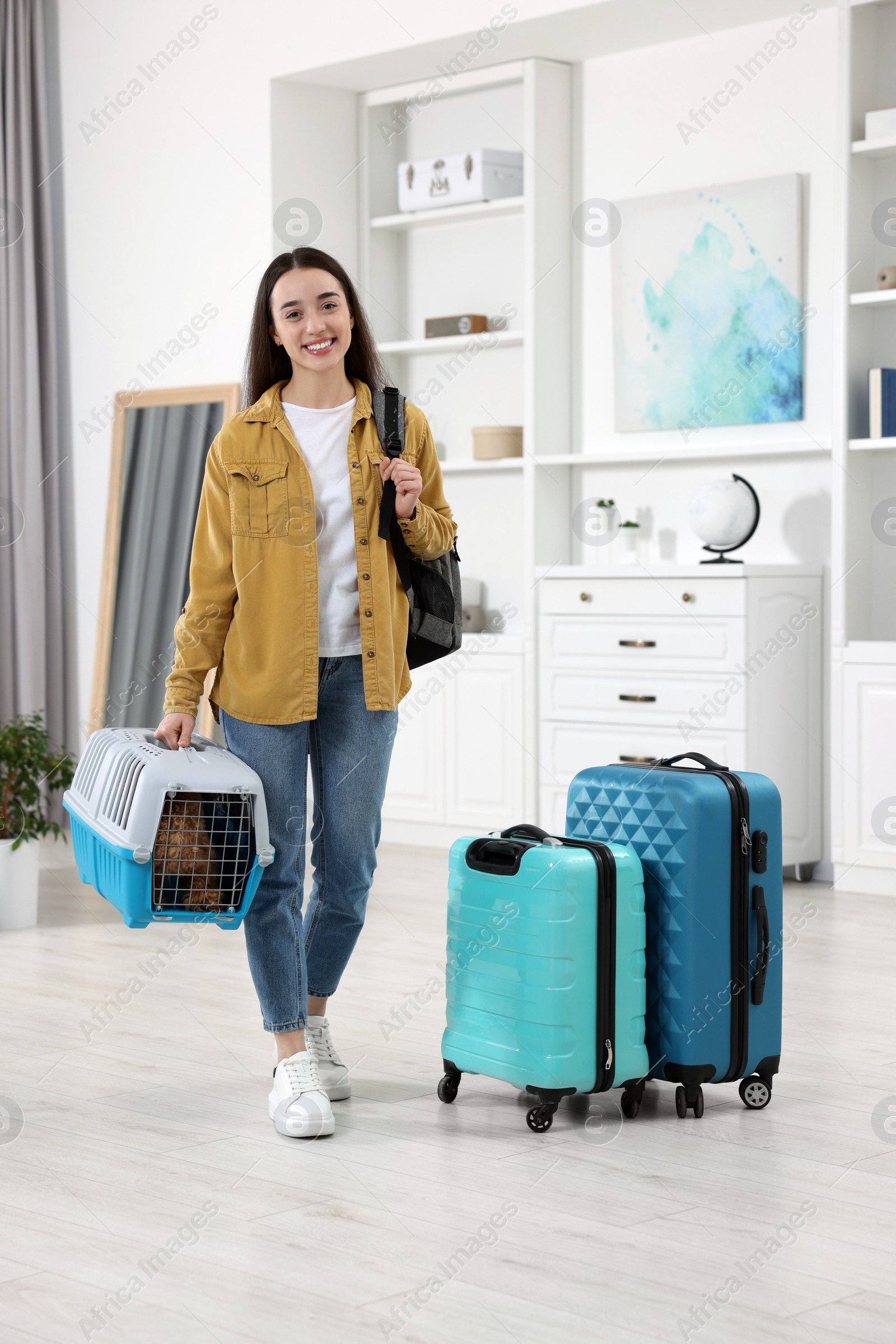 Photo of Travel with pet. Smiling woman with backpack holding carrier with dog at home