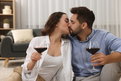 Photo of Passionate young couple with glasses of wine kissing at home