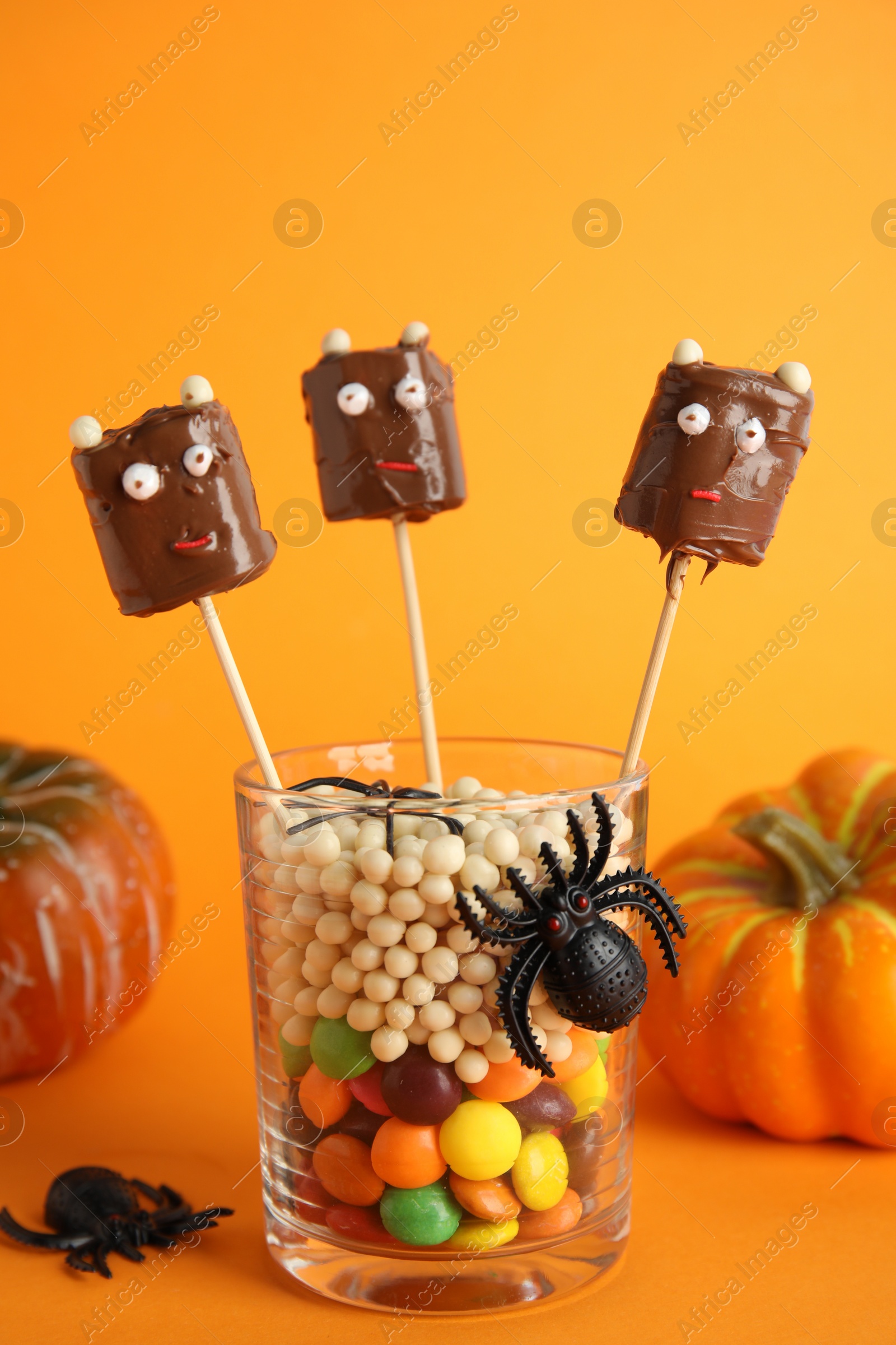 Photo of Delicious candies decorated as monsters on orange background. Halloween treat