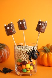 Photo of Delicious candies decorated as monsters on orange background. Halloween treat