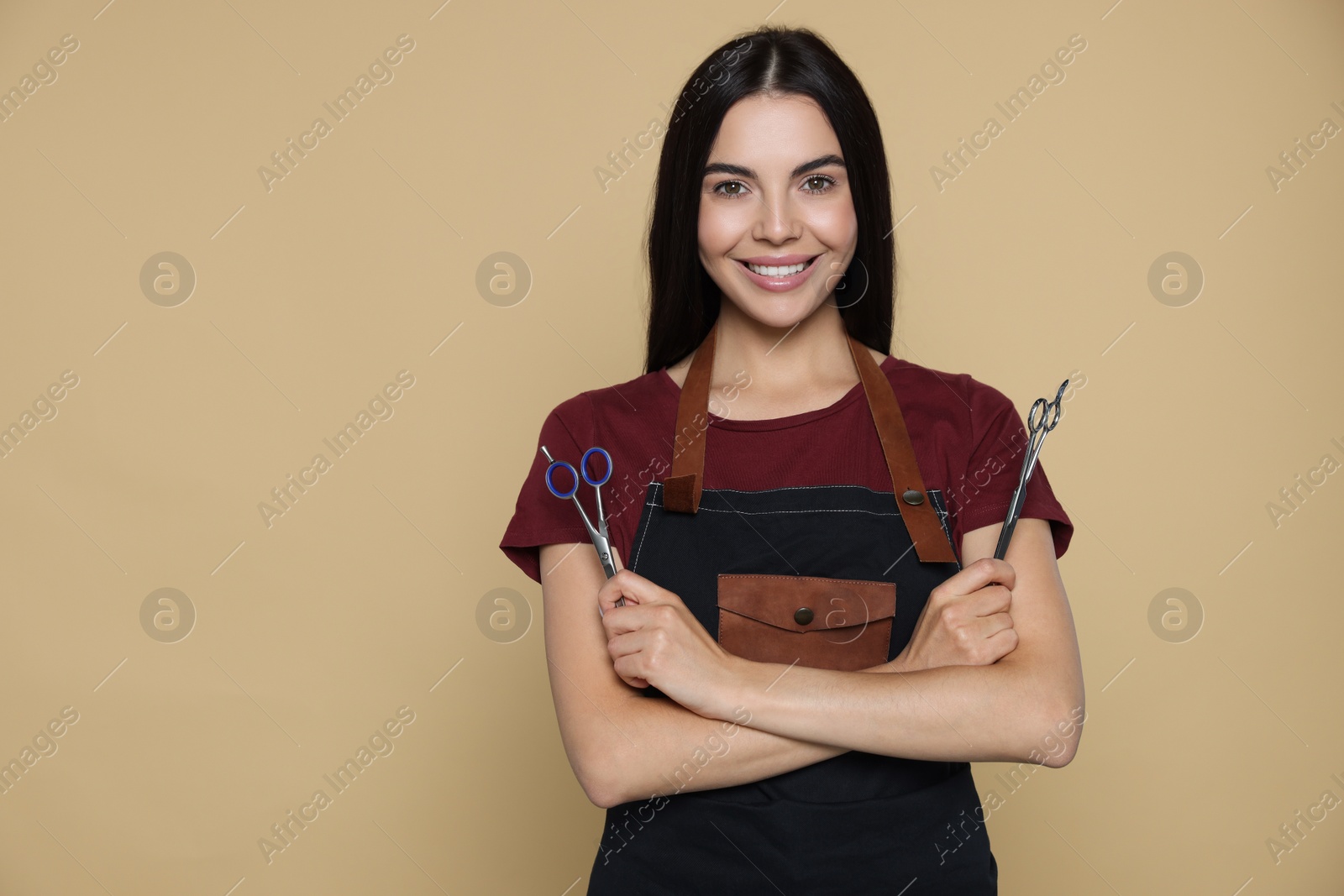 Photo of Portrait of happy hairdresser with professional scissors on beige background