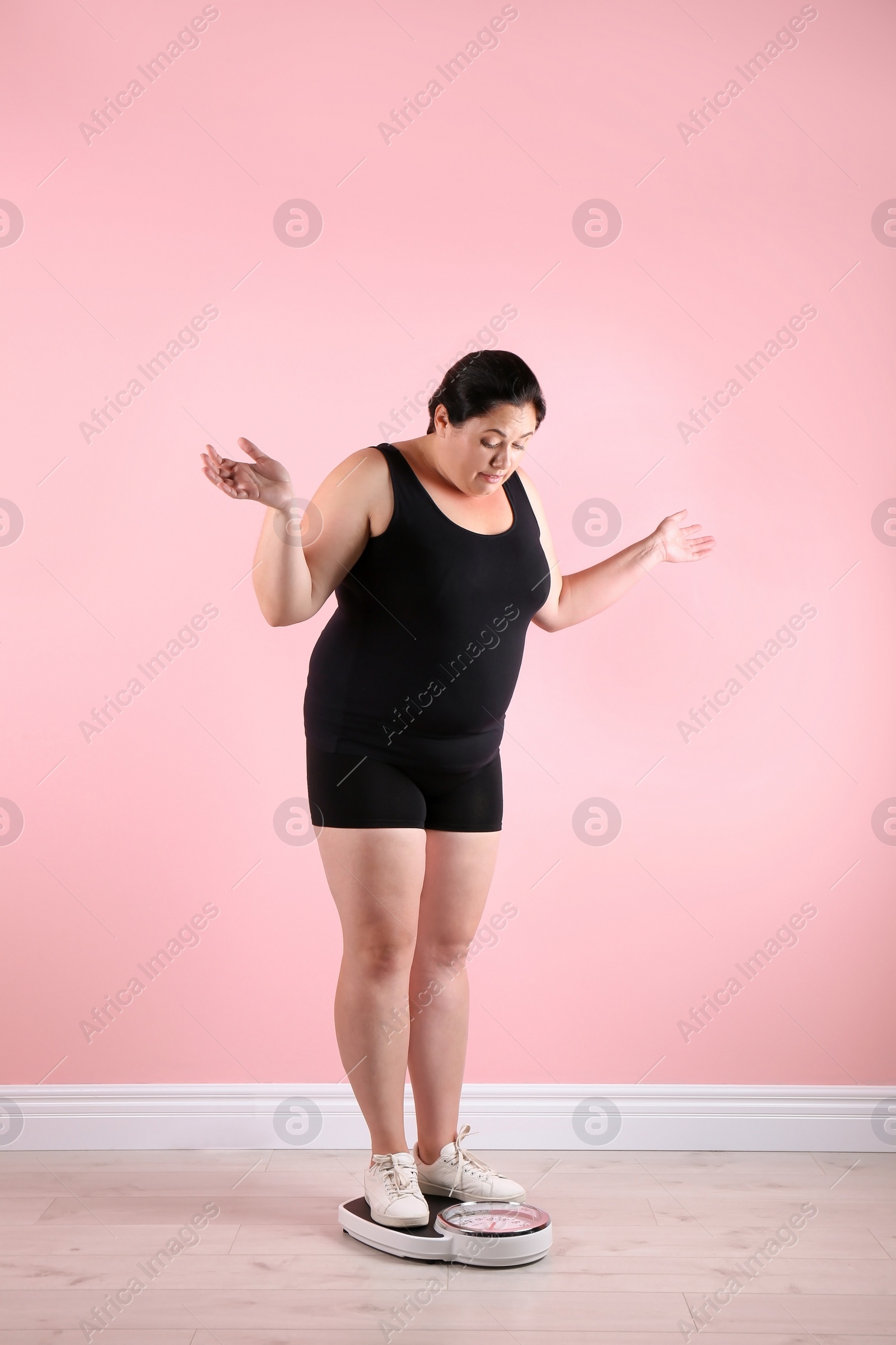 Photo of Overweight woman in sportswear using scales near color wall