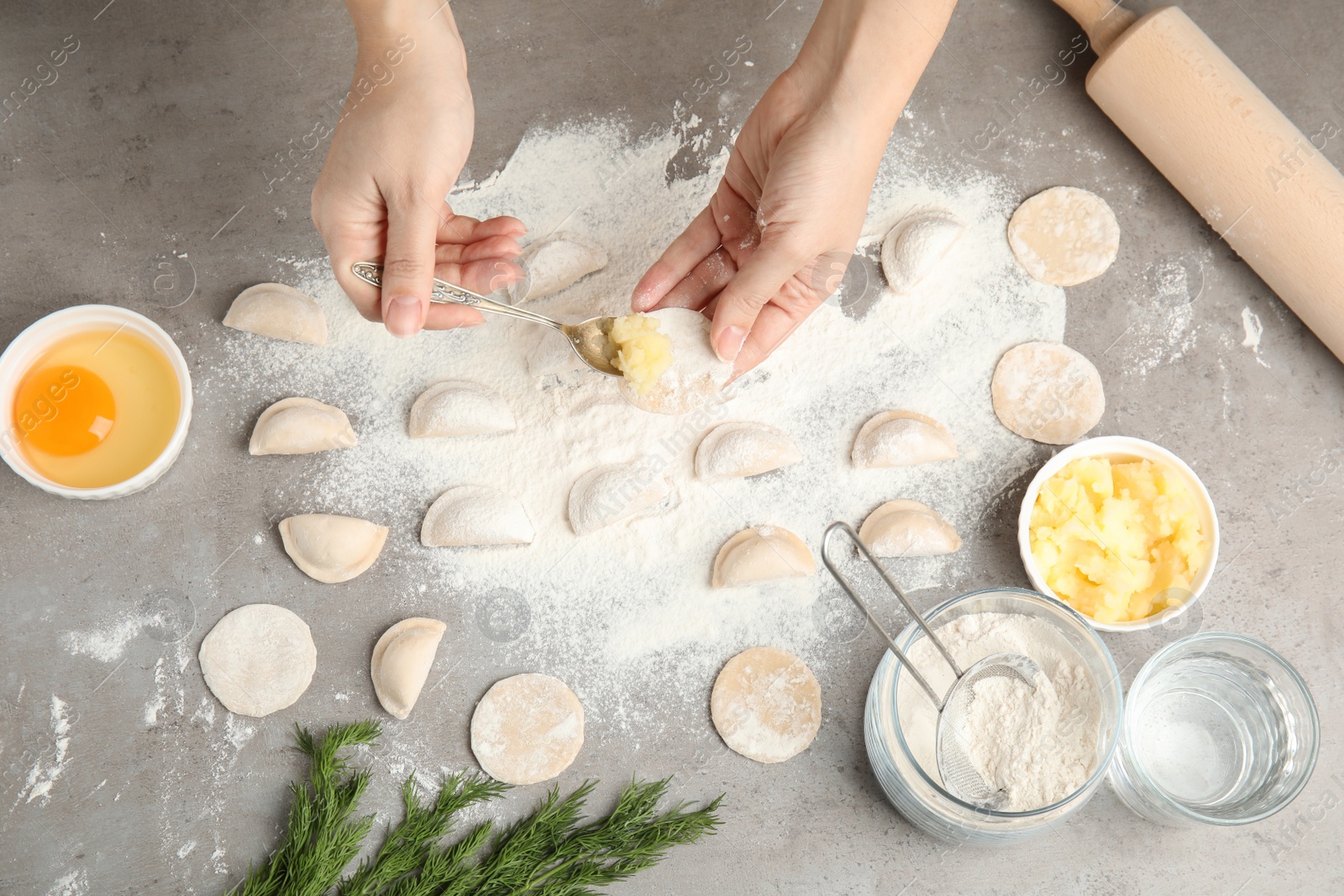 Photo of Woman cooking dumplings over grey table, top view