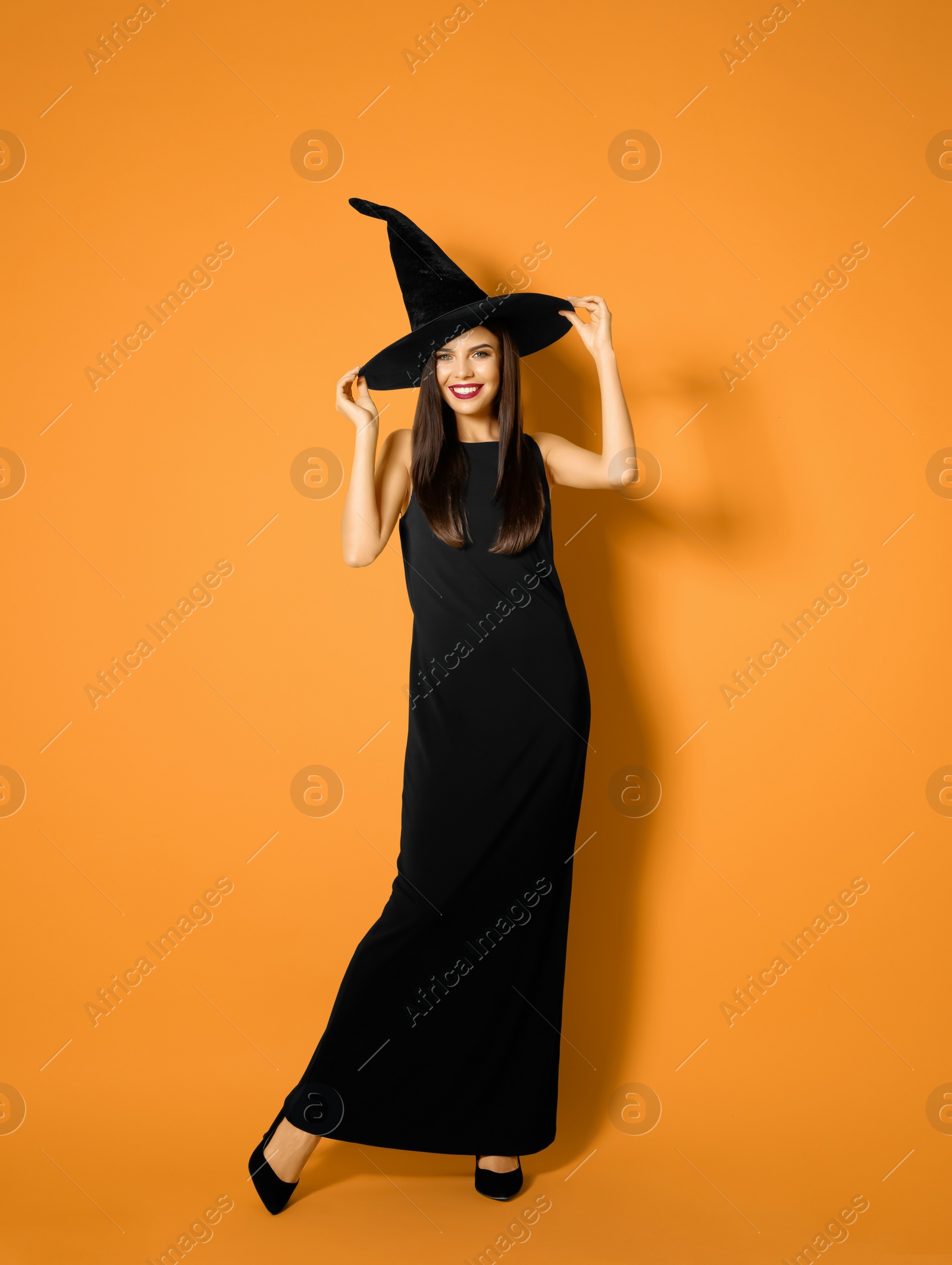 Photo of Beautiful woman wearing witch costume for Halloween party on yellow background