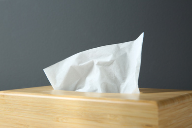 Photo of Wooden holder with paper tissues on dark background, closeup