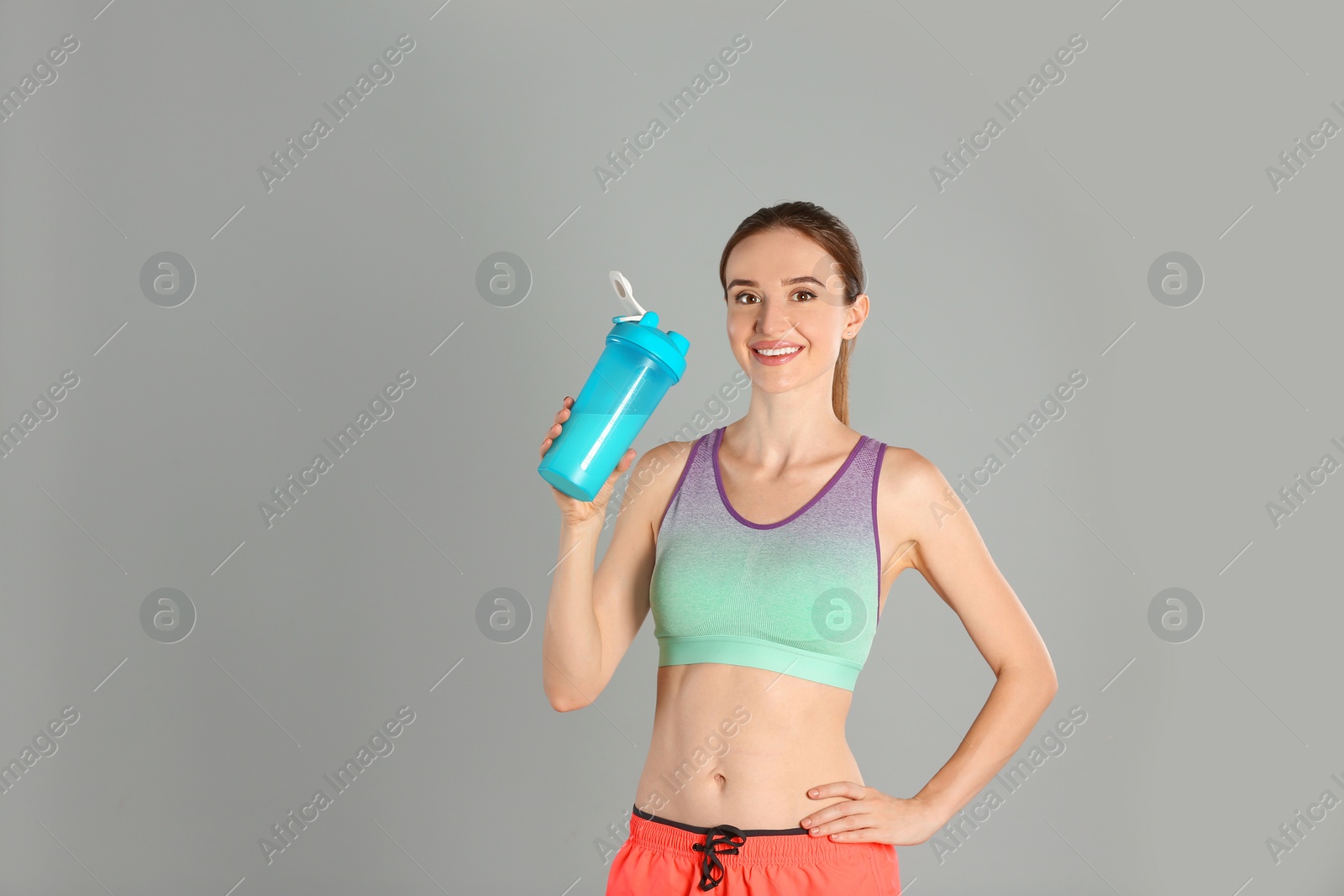 Photo of Athletic young woman with protein shake on light grey background. Space for text