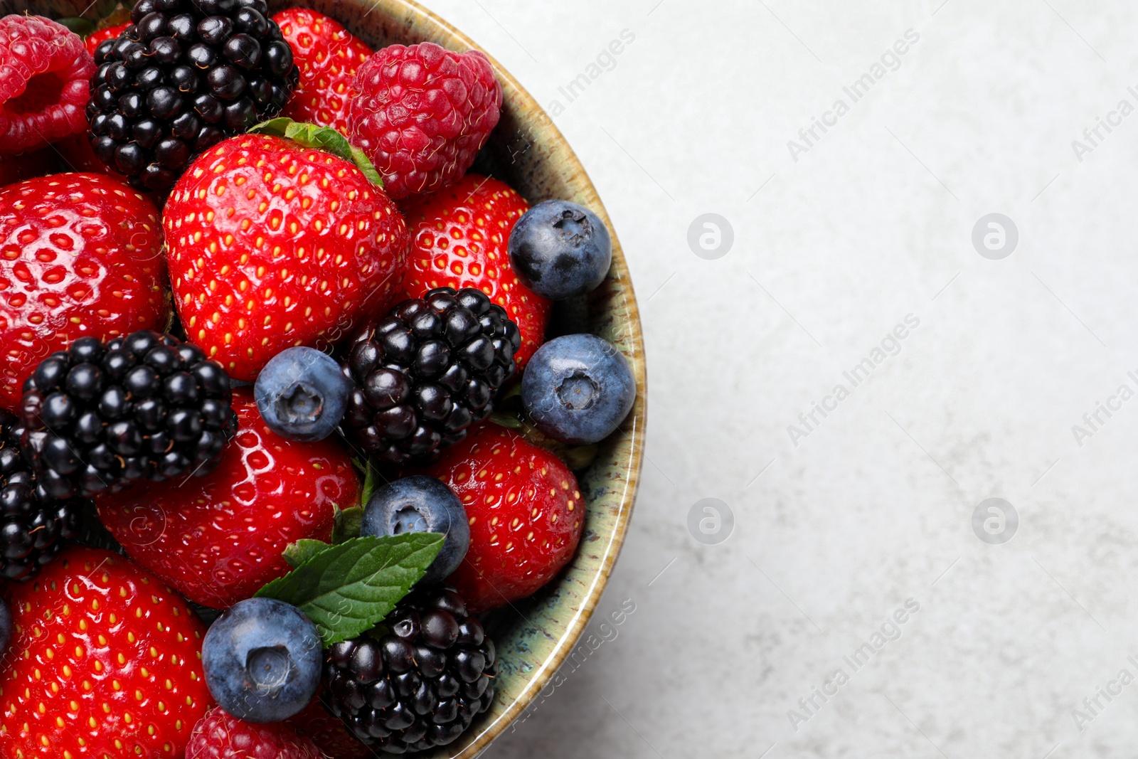 Photo of Different fresh ripe berries in bowl on light grey table, top view. Space for text