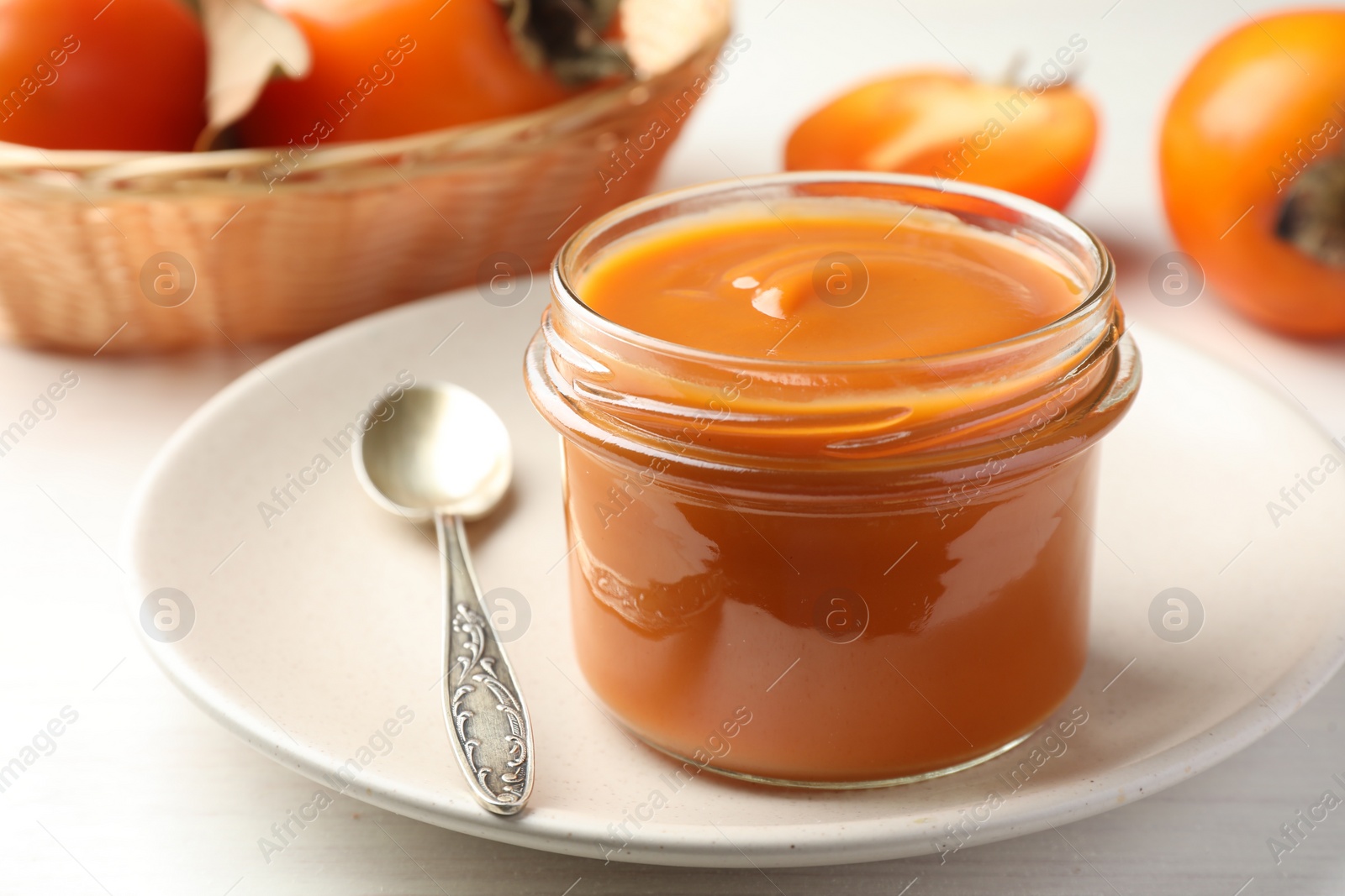 Photo of Delicious persimmon jam in glass jar served on white wooden table, closeup