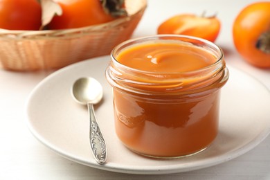 Delicious persimmon jam in glass jar served on white wooden table, closeup