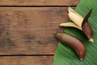 Photo of Delicious purple bananas and fresh leaf on wooden table, closeup. Space for text