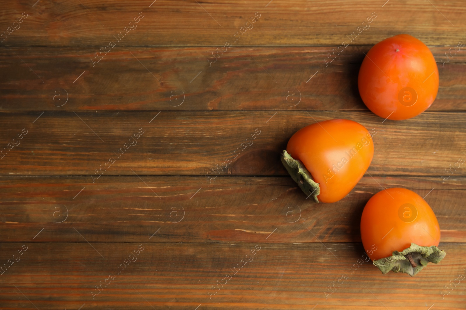 Photo of Tasty ripe persimmons on wooden table, flat lay. Space for text