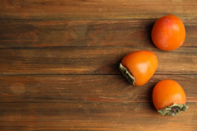 Photo of Tasty ripe persimmons on wooden table, flat lay. Space for text