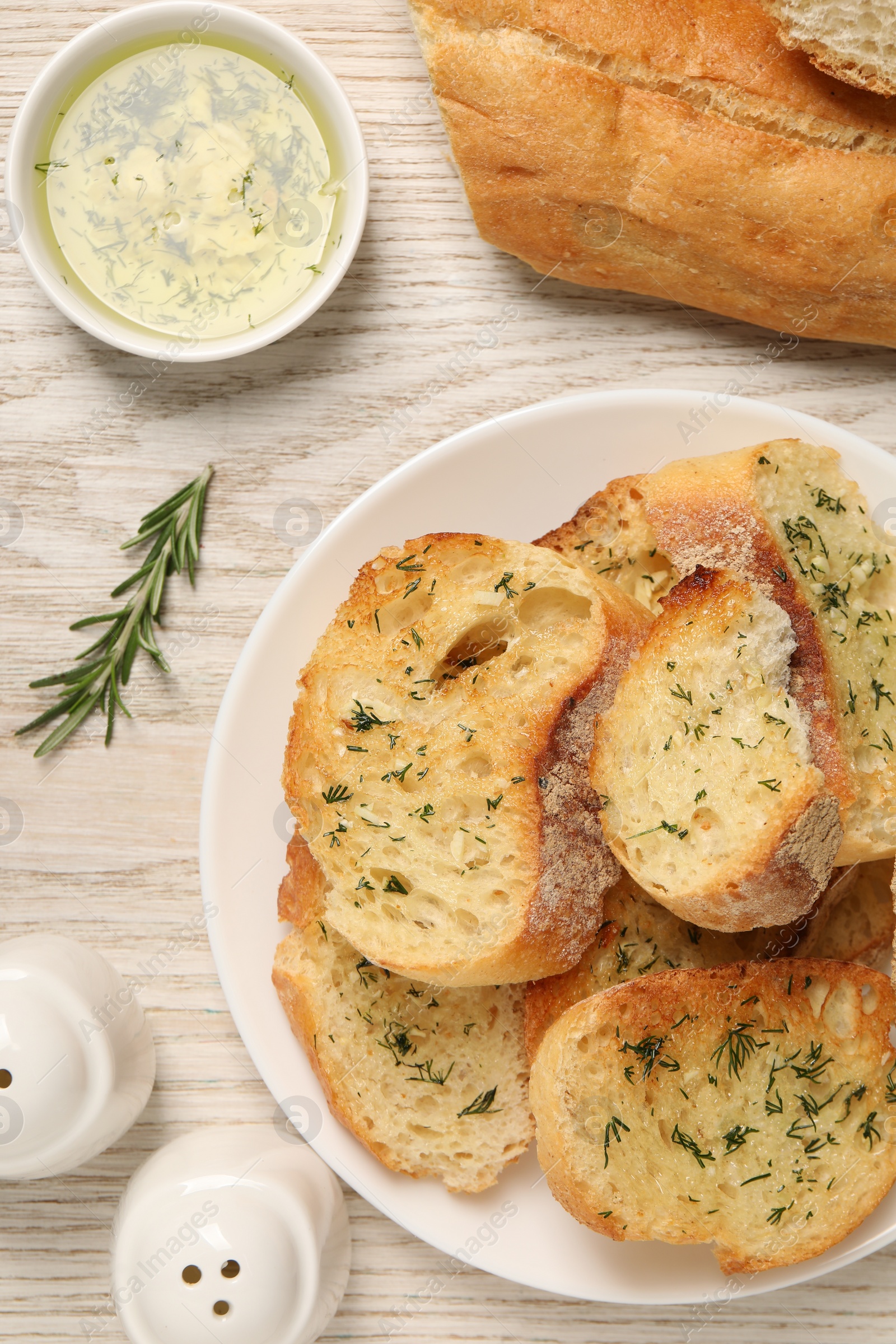 Photo of Tasty baguette with garlic served on white wooden table, flat lay