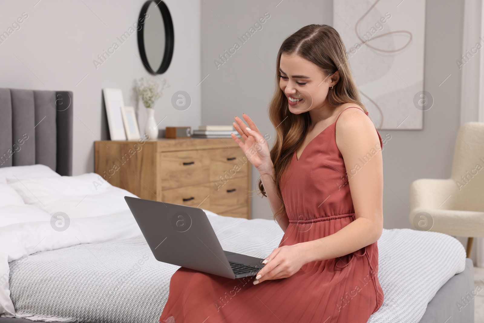 Photo of Happy woman having video chat via laptop on bed in bedroom