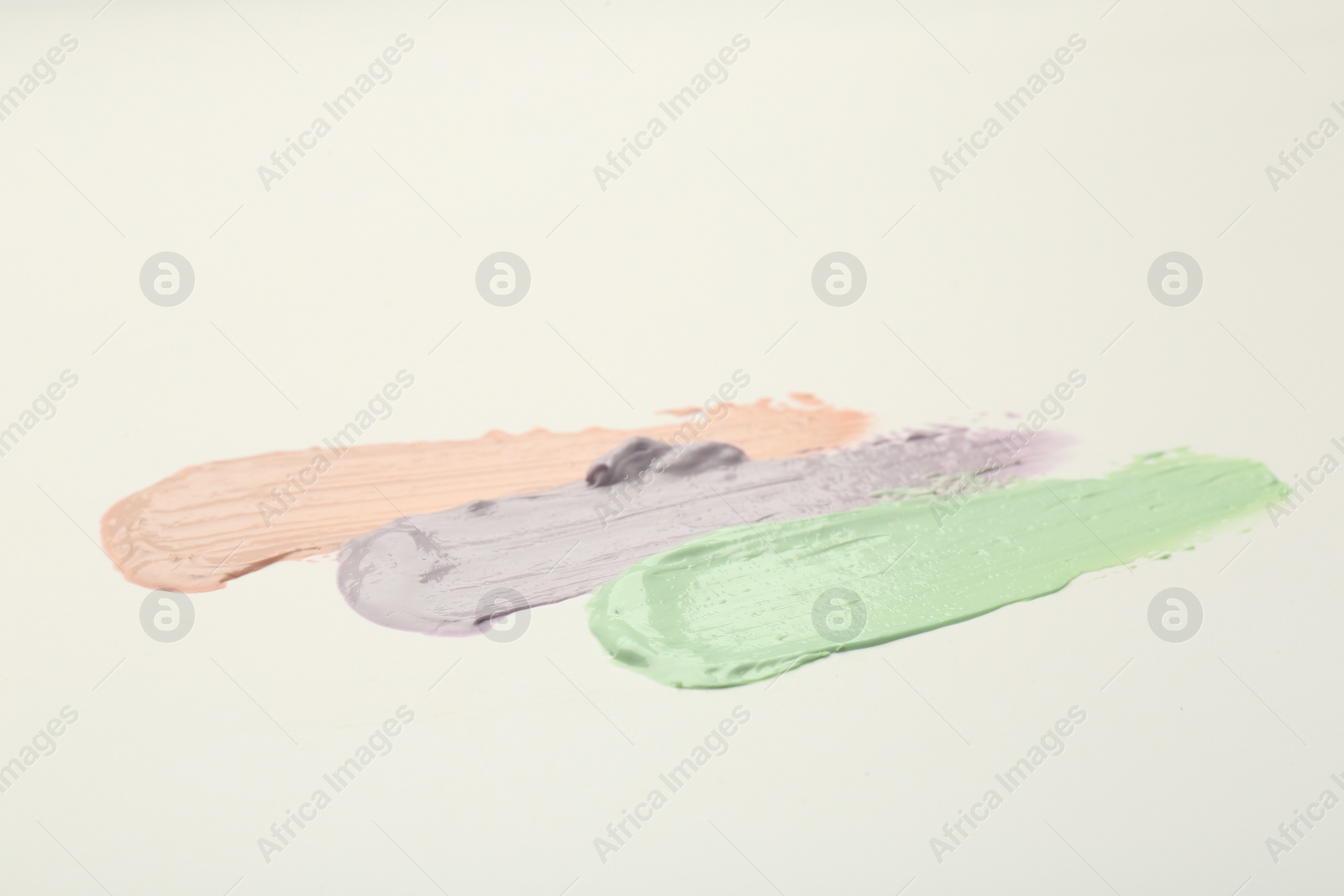 Photo of Strokes of pink, green and purple color correcting concealers on white background