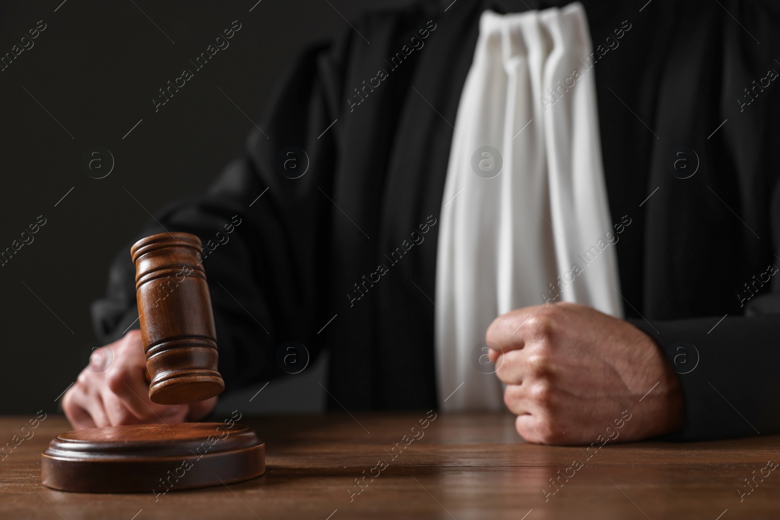 Photo of Judge with gavel sitting at wooden table against black background, closeup