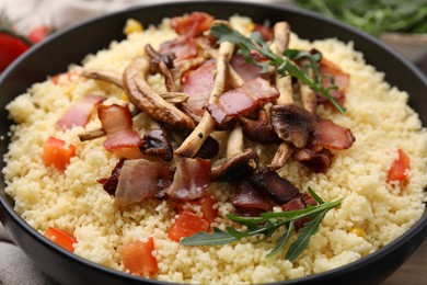 Tasty couscous with mushrooms and bacon in bowl on table, closeup