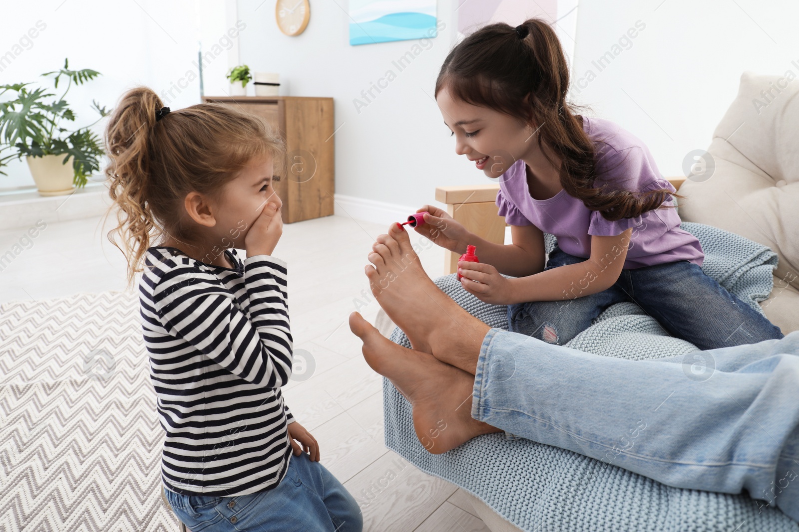 Photo of Cute little children applying polish on father's nails while he sleeping at home, closeup