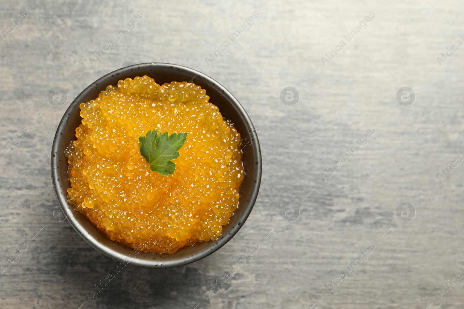 Photo of Fresh pike caviar and parsley in bowl on grey table, top view. Space for text