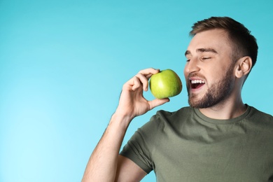 Photo of Young man with healthy teeth and apple on color background. Space for text