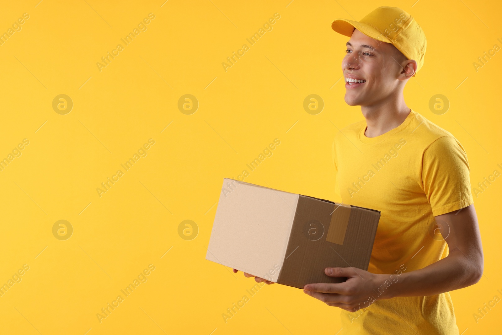 Photo of Happy courier with parcel on orange background. Space for text