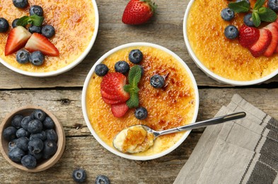 Flat lay composition with delicious creme brulee with berries and mint in bowls on wooden table