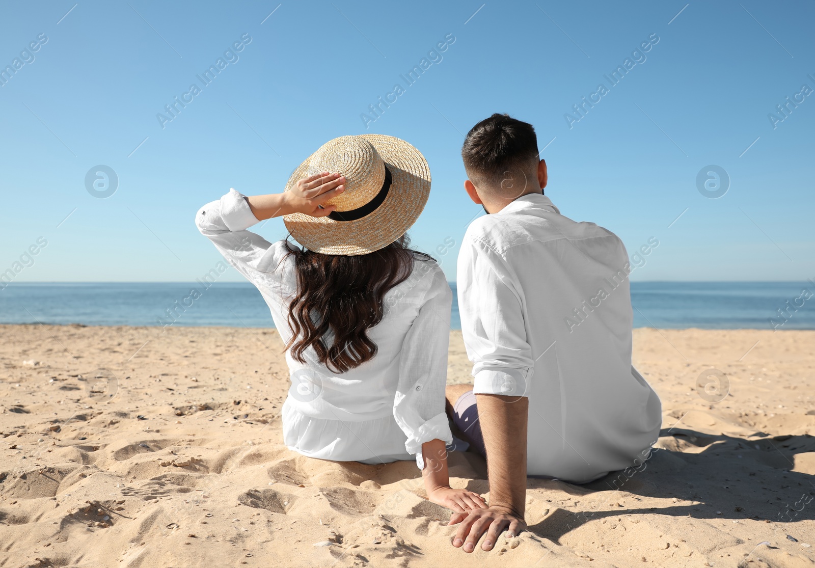 Photo of Young couple on beach near sea, back view. Honeymoon trip