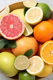 Different fresh citrus fruits and leaves in bowl on light table, top view