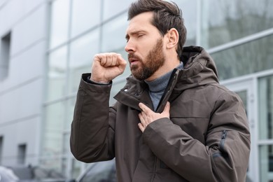 Photo of Sick man coughing on city street. Cold symptoms