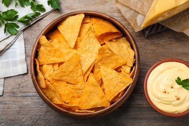 Photo of Delicious nachos and cheese sauce with parsley on wooden table, flat lay